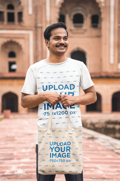 T-Shirt Mockup of a Happy Man Holding a Tote Bag Next to an Ancient Building