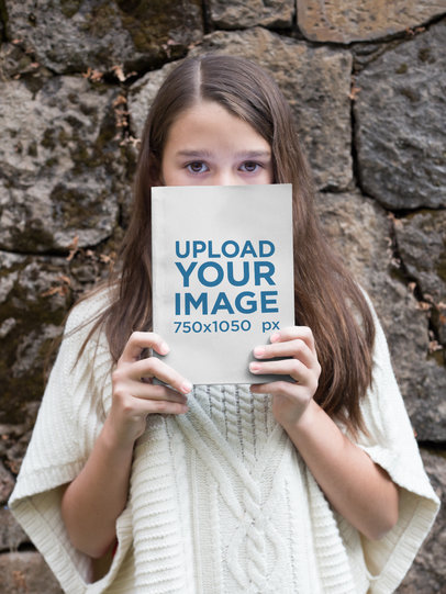 Little Girl Holding a Book Mockup Against her Face Outdoors