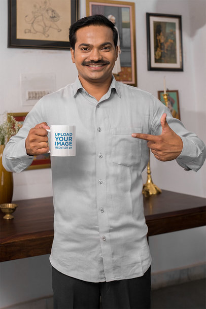 Mockup of a Man Pointing at His Coffee Mug and Smiling at Home