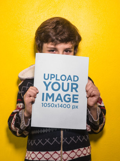 Boy Holding a Big Book Mockup Against a Yellow Wall a19218