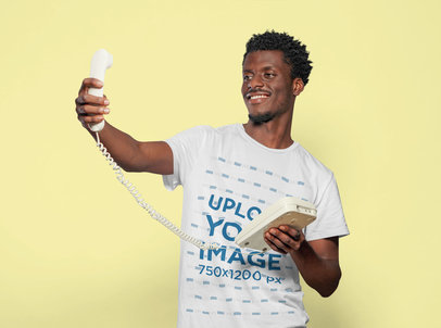 T-Shirt Mockup Featuring a Smiling Man Holding a Corded Phone in a Selfie Position
