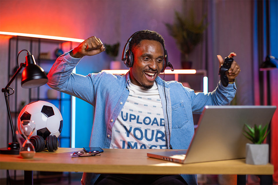 Round-Neck Tee Mockup Featuring a Happy Man Playing Virtual Soccer Games at Home