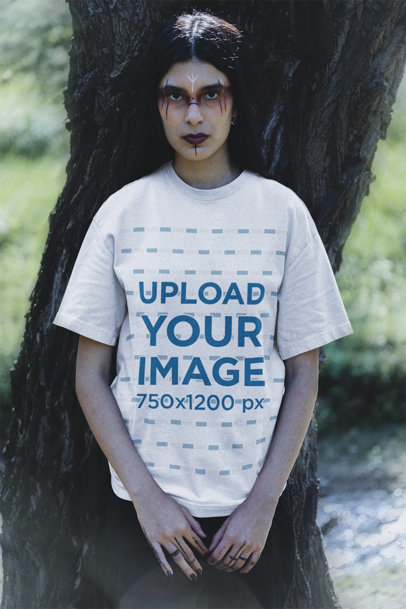 Oversized T-Shirt Mockup of a Woman with Tribal-Inspired Makeup Posing by a Tree