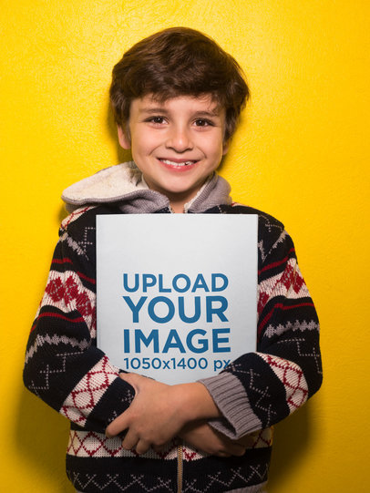 Happy Boy Holding a Book Mockup Against a Yellow Wall