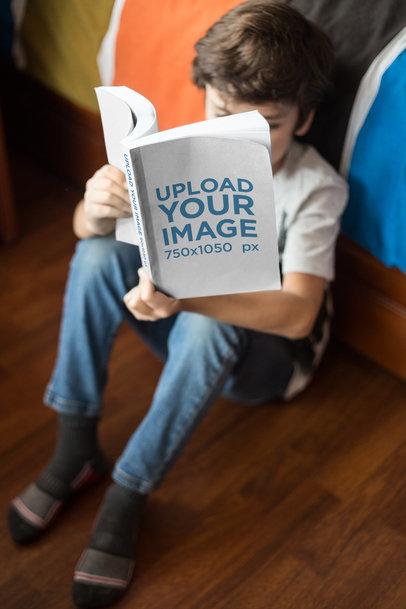 Boy Reading a Paperback Book Mockup Sitting Against his Bed