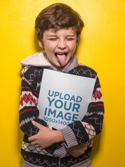 Boy Sticking His Tongue Out Holding a Book Mockup Against a Yellow Wall