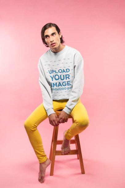 Man Wearing a Crewneck Sweater Mockup Sitting in a Pink Room a19675