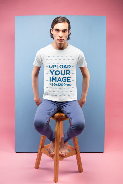 T-Shirt Mockup of a Man Sitting Against a Light Blue Rectangle in a Pink Room