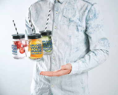 Mockup of a Man With a Denim Shirt Holding Transparent Mason Jars