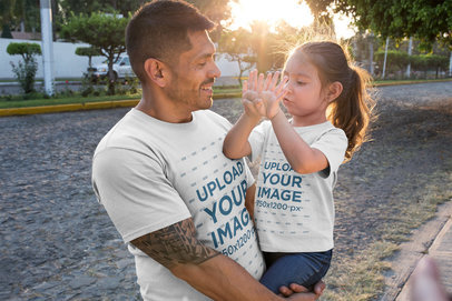 Dad and Daughter T-Shirt Mockup Featuring a Man Raising his Daughter on the Street