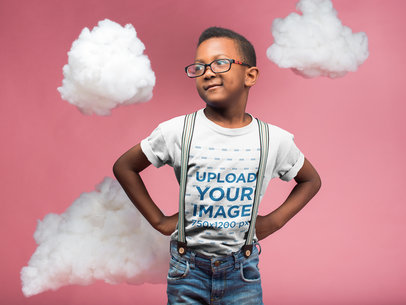 Kid Wearing a T-Shirt Mockup and Glasses while Standing in a Pink Room with Clouds