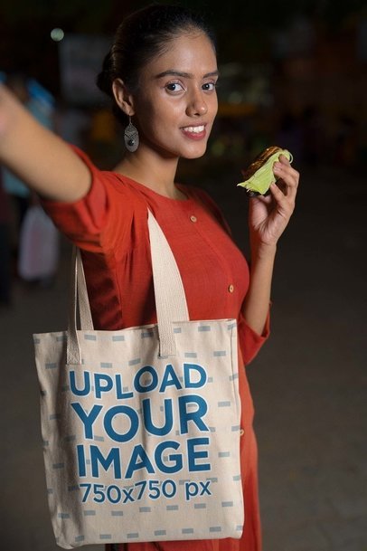 Tote Bag Mockup Featuring a Woman With an Indian Snack While Taking a Selfie