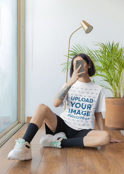 T-Shirt Mockup Featuring a Woman Taking a Photo With Her Phone