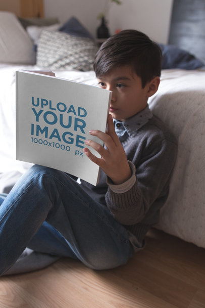 Boy Reading a Square Book Mockup Sitting Against his Bed