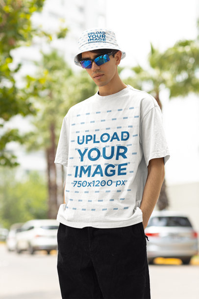T-Shirt Mockup of a Man with a Bucket Hat and Sunglasses Posing on a Street