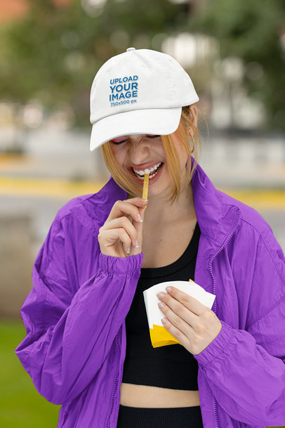 Dad Hat Mockup Featuring a Happy Woman Eating a French Fry