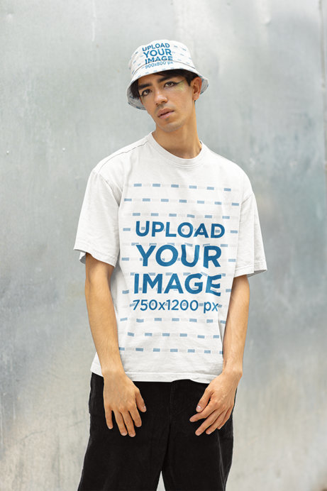 T-Shirt and Bucket Hat Mockup Featuring a Man Posing Against a Gray Wall
