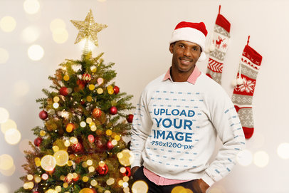 Sweatshirt Mockup of a Man with a Santa Hat Posing by a Xmas Tree