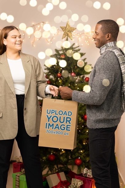 Mockup of a Man and a Woman Exchanging a Gift Bag in Front of a Xmas Tree