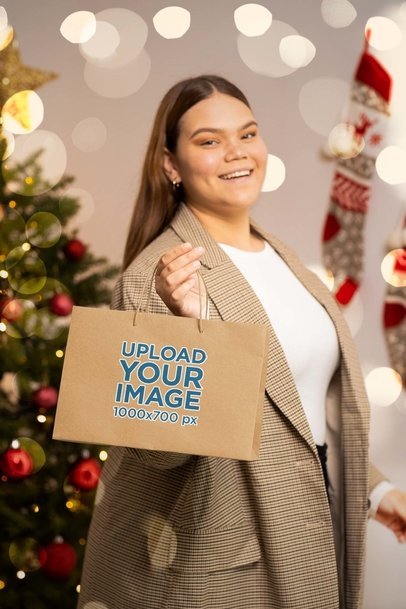 Mockup of a Happy Woman Holding a Gift Bag in a Christmas-Decorated Room