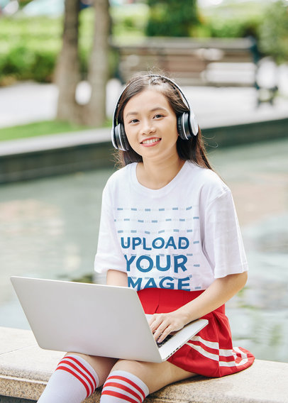 T-Shirt Mockup Featuring a Smiling Teenage Girl Using Headphones and a Laptop
