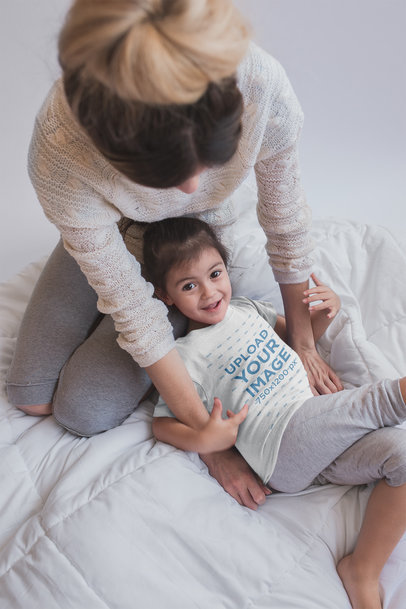 Little Girl Wearing a Tshirt Mockup while Playing with her Mom on the Bed