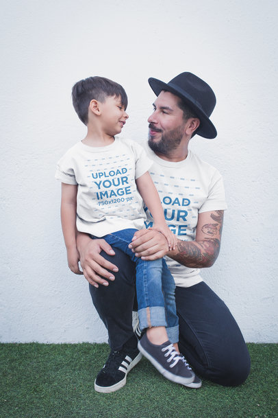 Father and Son Wearing T-Shirts Mockup Against a White Wall