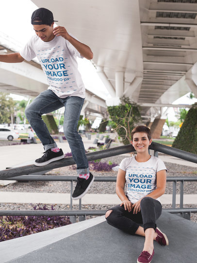 Boy and Girl Wearing T-Shirts Mockup While Jumping Under a Bridge a16434