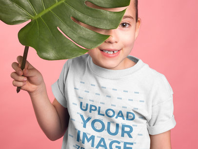 Girl Wearing a Tshirt Mockup Hiding Behind a Big Leaf