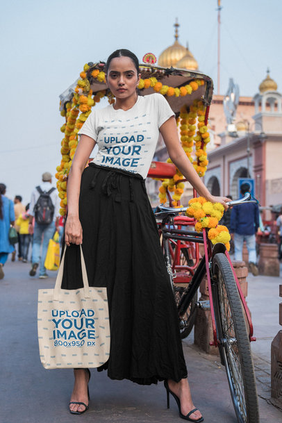 T-Shirt Mockup of a Woman Posing with a Tote Bag Next to a Decorated Bike