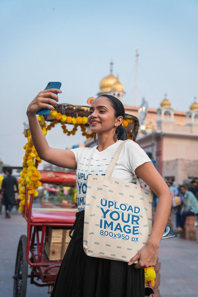 Gildan Tee Mockup Featuring a Woman Carrying a Tote Bag and Taking a Selfie