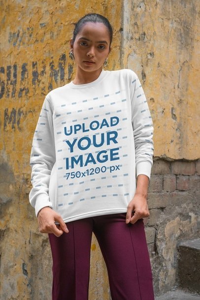 Mockup of a Woman in a Crewneck Sweatshirt Posing by a Distressed Wall