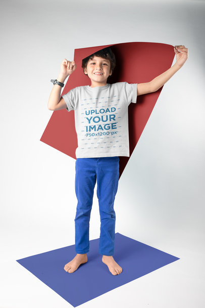 Kid Holding a Paper Wearing a T-Shirt Mockup in a White Room