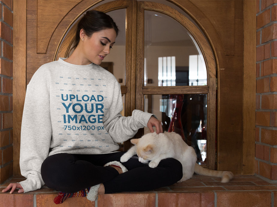 Woman Wearing a Crewneck Sweater Mockup Petting her Cat Against a Window