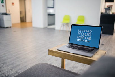 Mockup of a MacBook Pro Resting on a Small Table at an Office