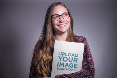 Happy Woman Holding a Book Mockup in a Grey Room