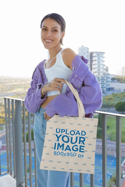 Tote Bag Mockup Featuring a Smiling Woman Posing for a TikTok by a Balcony
