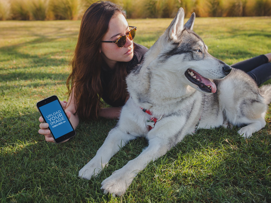 Woman Holding an iPhone 8+ Mockup Lying with her Dog at the Park