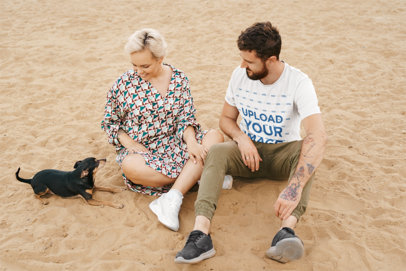 T-Shirt Mockup of a Man with a Tattooed Arm Sitting on the Beach Next to Her Girlfriend