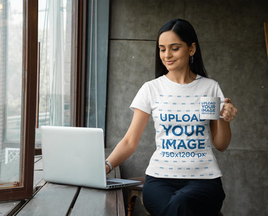 Gildan Tee Mockup of a Woman Using Her Laptop and Holding an 11 oz Coffee Mug