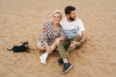 T-Shirt Mockup Featuring a Joyful Couple Sitting on the Beach with Their Dog