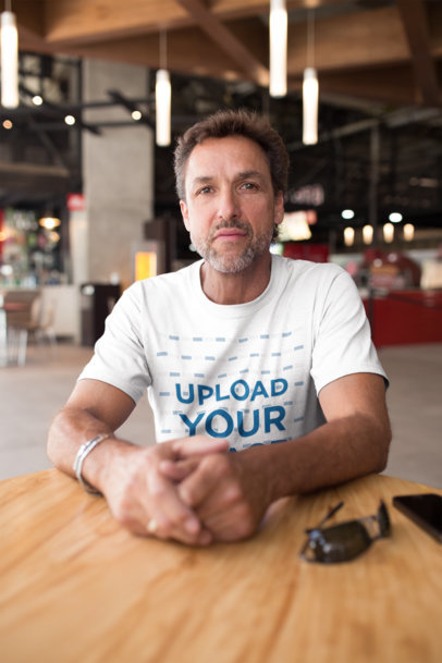 Middle-Aged Man Wearing a T-Shirt Mockup Sitting at a Cafe