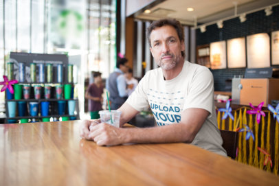 Middle Aged Man Wearing a T-Shirt Mockup Having an Iced Latte at a Coffee Shop