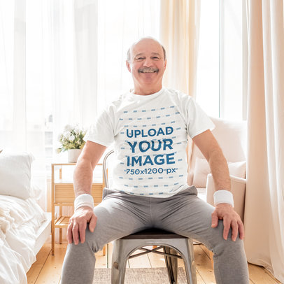 Rounded-Neck Tee Mockup of a Smiling Senior Man Sitting on a Chair at Home