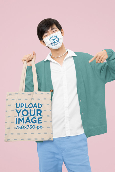 Mockup of a Man with a Face Mask Pointing at His Sublimated Tote Bag