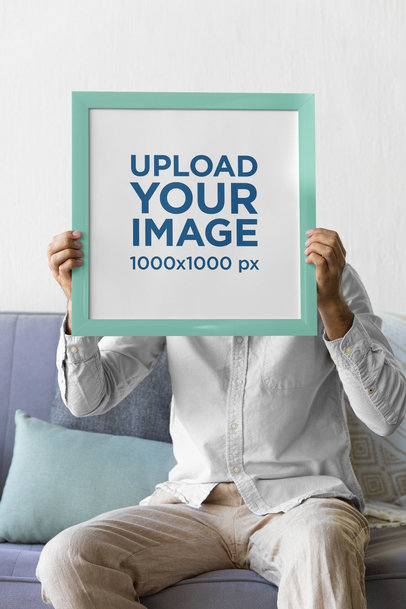 Mockup of a Man Holding a Squared Art Print While Sitting on a Couch