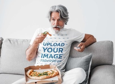 T-Shirt Mockup Featuring a Bearded Senior Man Eating Pizza at Home
