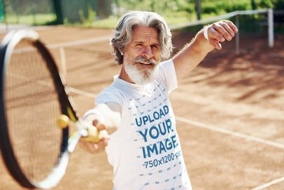 T-Shirt Mockup of a Senior Man Holding a Tennis Racket on a Court