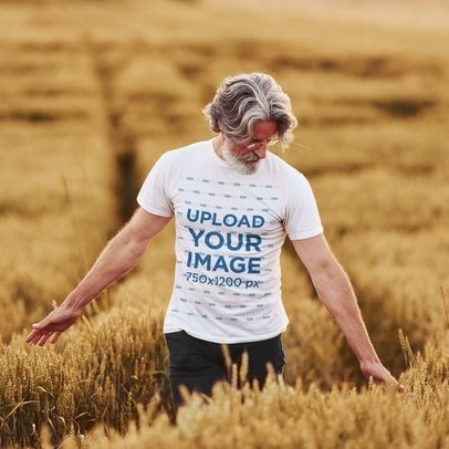 T-Shirt Mockup Featuring a Senior Man Walking Through a Wheat Field