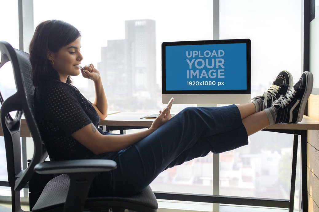 Woman Checking her Phone at the Office Near an iMac Mockup